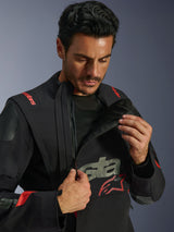 Alpinestars Halo Pro Drystar® XF Laminated Jacket, Black Dark Shadow, model demonstrating the modular ventilation system by unzipping the asymmetrical front chest panel, adventure touring jacket with red Alpinestars branding and technical mesh detailing.