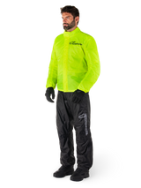 Man wearing Alpinestars Hurricane Rain V2 Jacket in Yellow Fluo and Hurricane Rain V2 Pants in Black, high-visibility waterproof motorcycle rain gear, featuring reflective logos on the chest and thigh, complete outfit with black gloves and boots.
