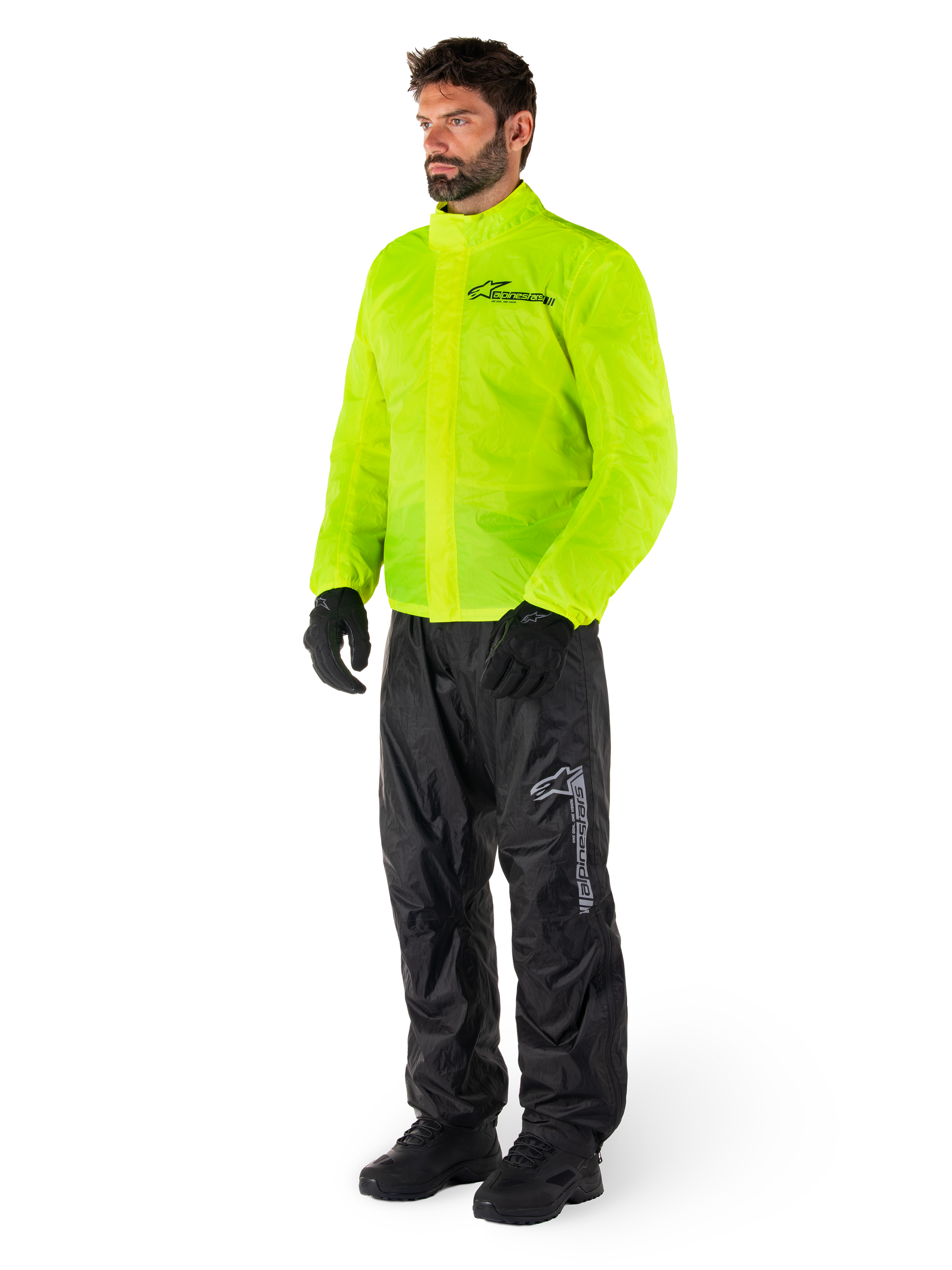 Man wearing Alpinestars Hurricane Rain V2 Jacket in Yellow Fluo and Hurricane Rain V2 Pants in Black, high-visibility waterproof motorcycle rain gear, featuring reflective logos on the chest and thigh, complete outfit with black gloves and boots.