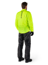 Person from the back wearing Alpinestars Hurricane Rain V2 Jacket in Yellow Fluo and Hurricane Rain V2 Pant in Black, vertical logo on jacket back, waterproof motorcycle rain gear with black gloves and boots