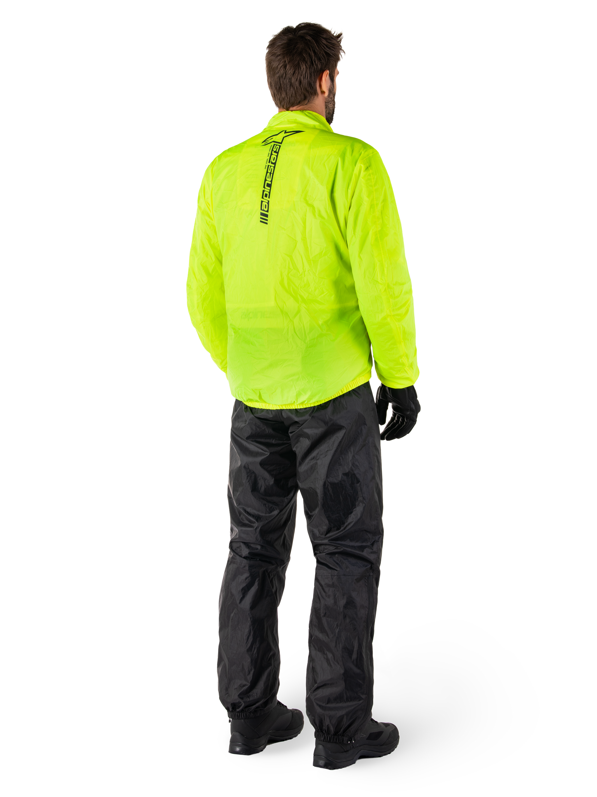 Person from the back wearing Alpinestars Hurricane Rain V2 Jacket in Yellow Fluo and Hurricane Rain V2 Pant in Black, vertical logo on jacket back, waterproof motorcycle rain gear with black gloves and boots