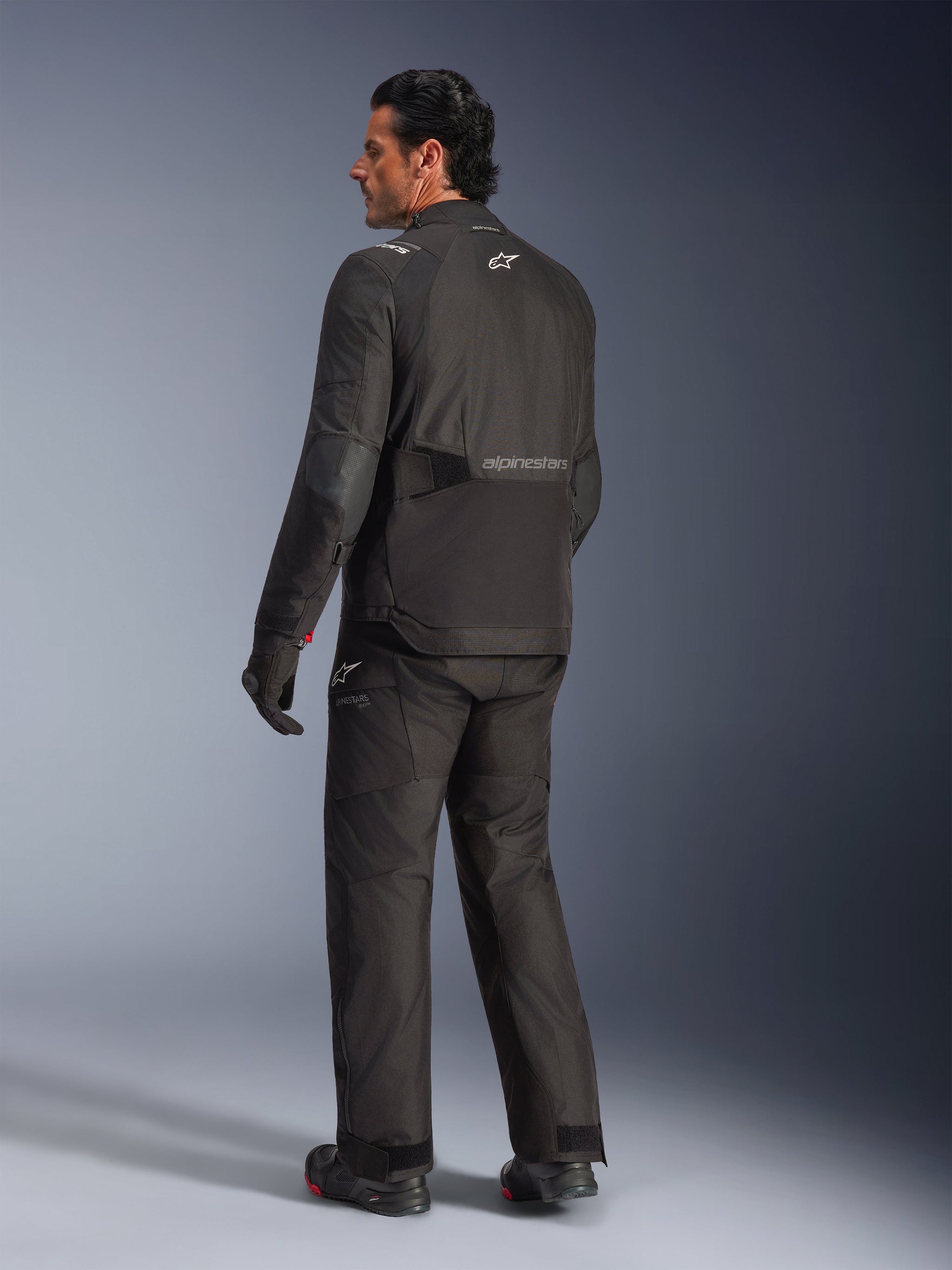 Alpinestars Andes V4 Drystar® Jacket, Black, back view of rider in complete motorcycle gear, textile adventure jacket featuring Alpinestars branding on the back, worn with matching black pants and boots, all-weather road and adventure riding style