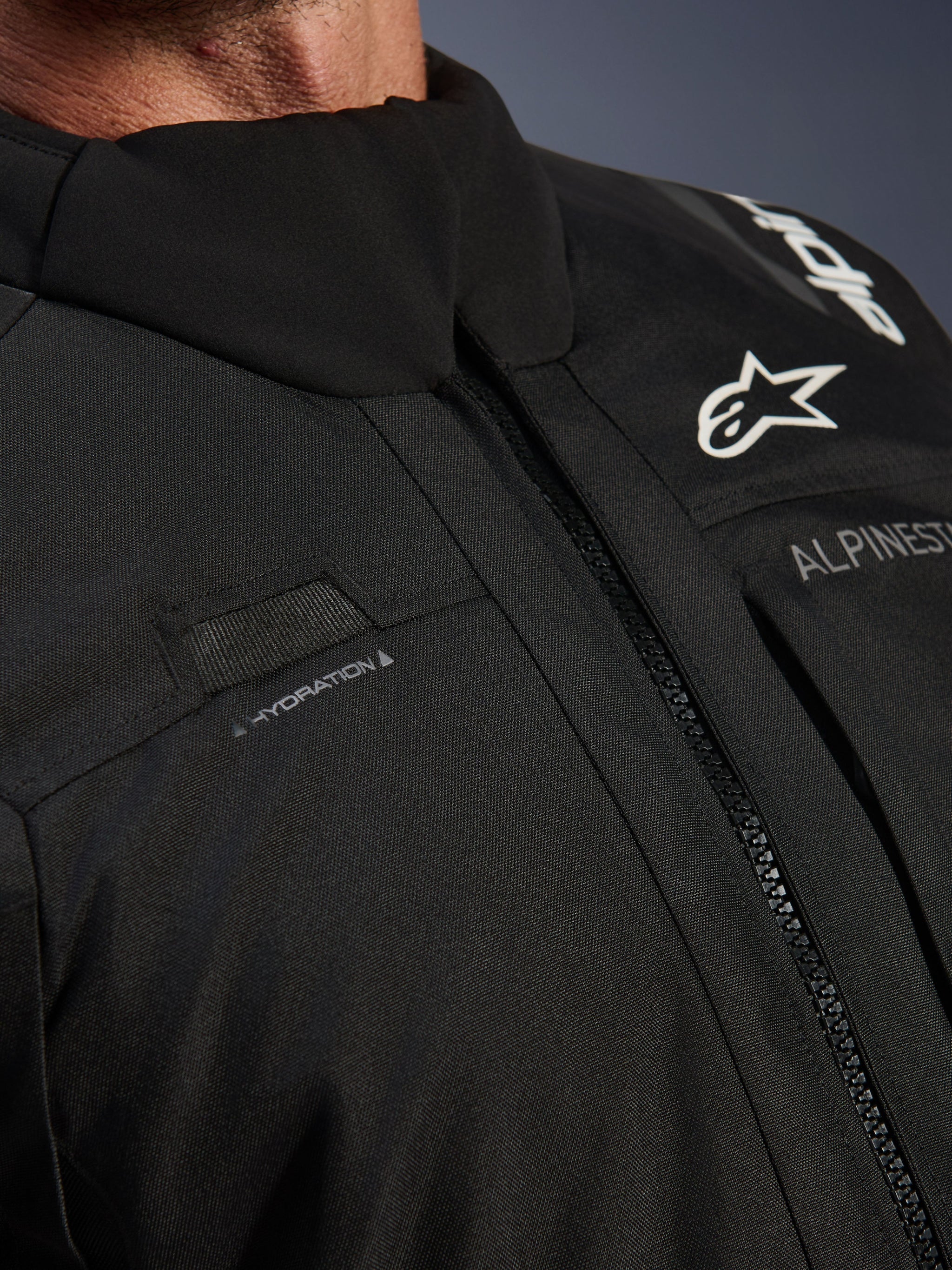 Alpinestars Andes V4 Drystar® Jacket, Black, close-up of chest detail featuring hydration hose loop, waterproof VISLON® front zipper, and Alpinestars logo on durable textile material