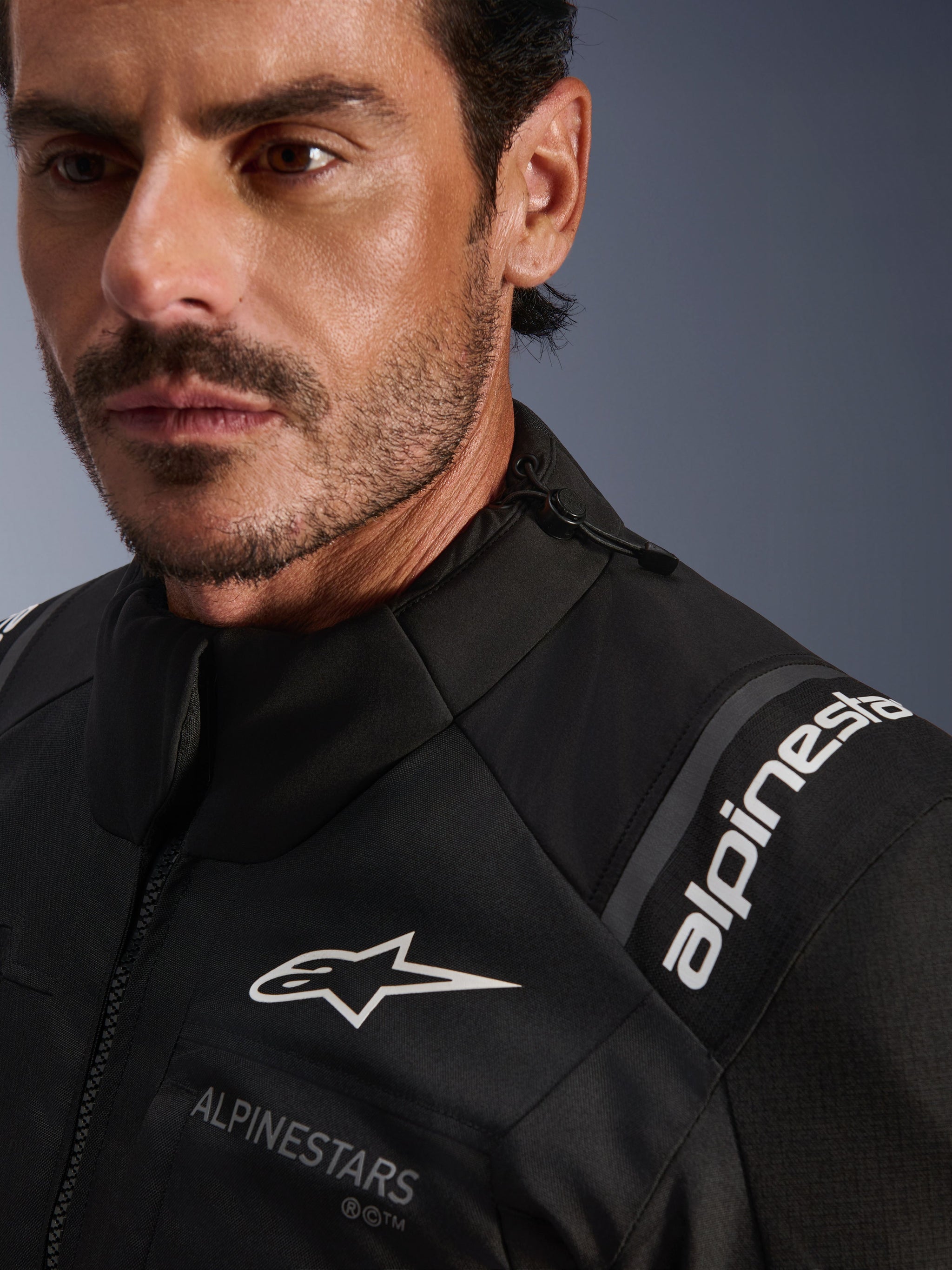 Alpinestars Andes V4 Drystar® Jacket, Black textile motorcycle jacket, close-up detail worn by a man, featuring white Alpinestars chest and shoulder logos, adjustable collar drawstring, and high-performance adventure-touring design.