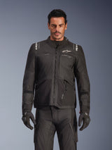 Male model wearing the Alpinestars Andes V4 Drystar® Jacket in Black, adventure touring motorcycle jacket, paired with matching black riding pants and gloves, featuring waterproof zippers and white Alpinestars branding on the chest and shoulders, studio shot for all-weather riding gear.