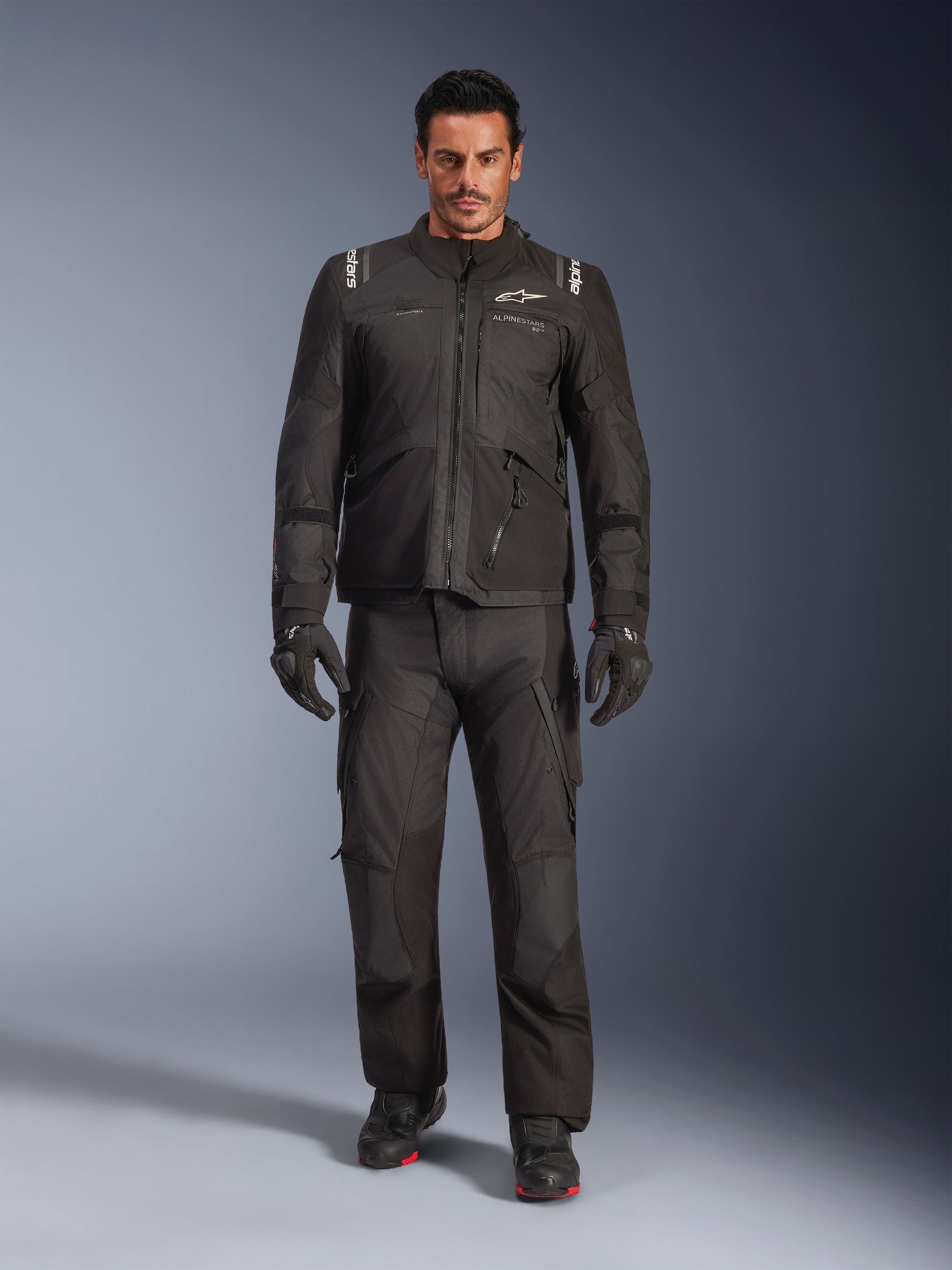 Male model wearing the Alpinestars Andes V4 Drystar® Jacket in Black, paired with matching adventure motorcycle pants, black gloves, and black boots, full-body studio shot showcasing technical all-weather touring gear with Alpinestars branding.