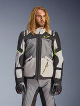 Alpinestars Andes V4 Drystar Jacket, Adventure Touring Motorcycle Jacket, Dark Gray and Ice Gray with Neon Yellow accents, worn by a model with matching pants and gloves, multi-pocket textile design for all-weather riding
