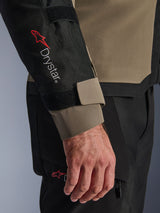 Close-up of the Alpinestars Andes V4 Drystar® Jacket in Walnut and Black, featuring the red Drystar® logo on the forearm and an adjustable cuff strap, part of a technical adventure motorcycle outfit.