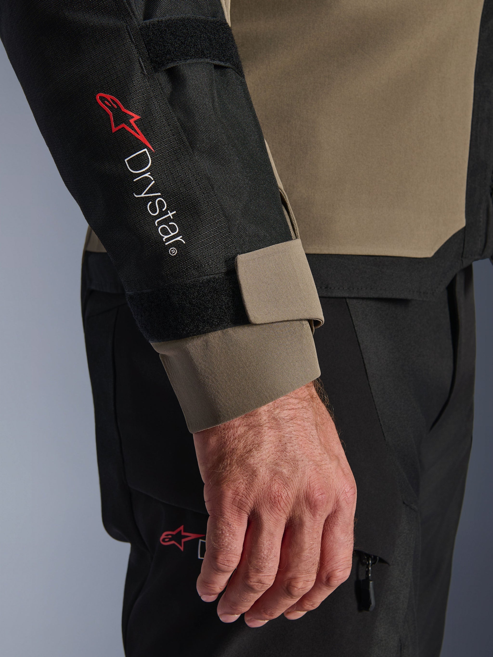 Close-up of the Alpinestars Andes V4 Drystar® Jacket in Walnut and Black, featuring the red Drystar® logo on the forearm and an adjustable cuff strap, part of a technical adventure motorcycle outfit.