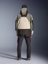 Rear view of a rider wearing the Alpinestars Mospher Waterproof Jacket in Fur Gray Black Ice, tactical-inspired parka with gray, black, and cream color-blocking, features a hood with orange strap detail, paired with black cargo pants.