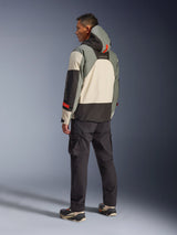 Alpinestars Mospher Waterproof Jacket in Fur Gray Black Ice, back view of a model wearing a tactical motorcycle parka with cream, gray, and black panels, featuring red accents and a hood, paired with black cargo pants and technical boots