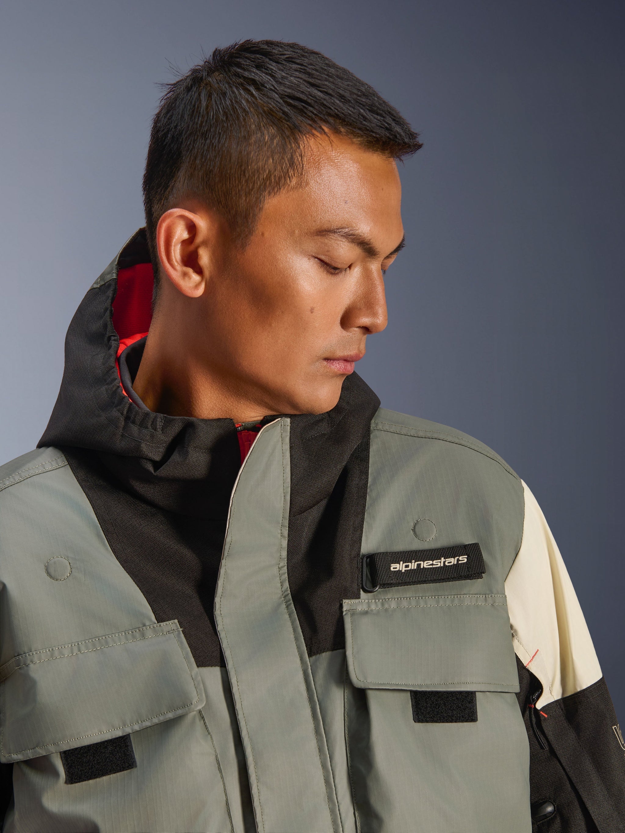 Alpinestars Mospher WP Jacket, Waterproof Motorcycle Parka, Fur Gray Black Ice, close-up of model wearing hooded jacket with utility pockets, black alpinestars logo tab, and tactical design with red interior lining