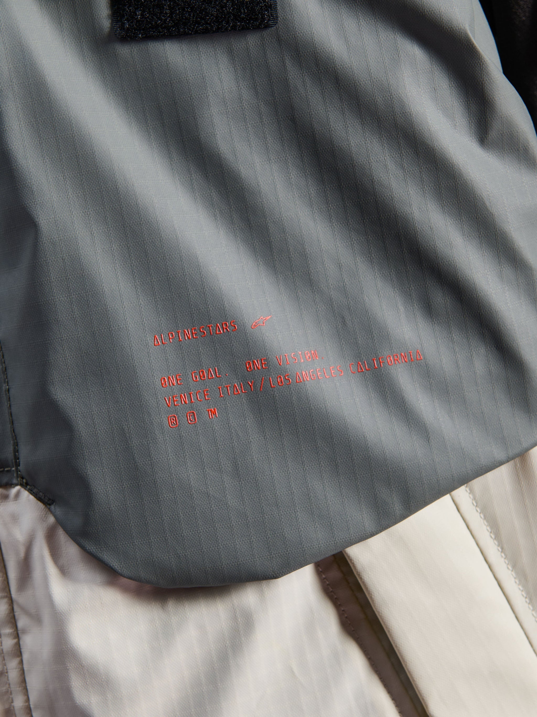 Alpinestars Mospher Waterproof Jacket, Motorcycle Parka, Fur Gray and Black Ice, detail of technical ripstop fabric with red Alpinestars branding and slogan, highlighting durable construction and urban tactical design