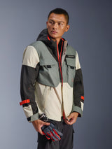 Alpinestars Mospher Waterproof Jacket in Fur Gray Black Ice, multi-panel textile parka with gray, black, and off-white sections, featuring bright red zipper and strap accents, tactical-inspired design with hood and utility pockets, worn by a model holding motorcycle gloves.