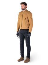 Male rider wearing the Alpinestars Clayton WR Jacket in Utility Brown Light Gold, urban contemporary motorcycle jacket with quilted shoulder details, styled with black pants, black gloves, and brown boots