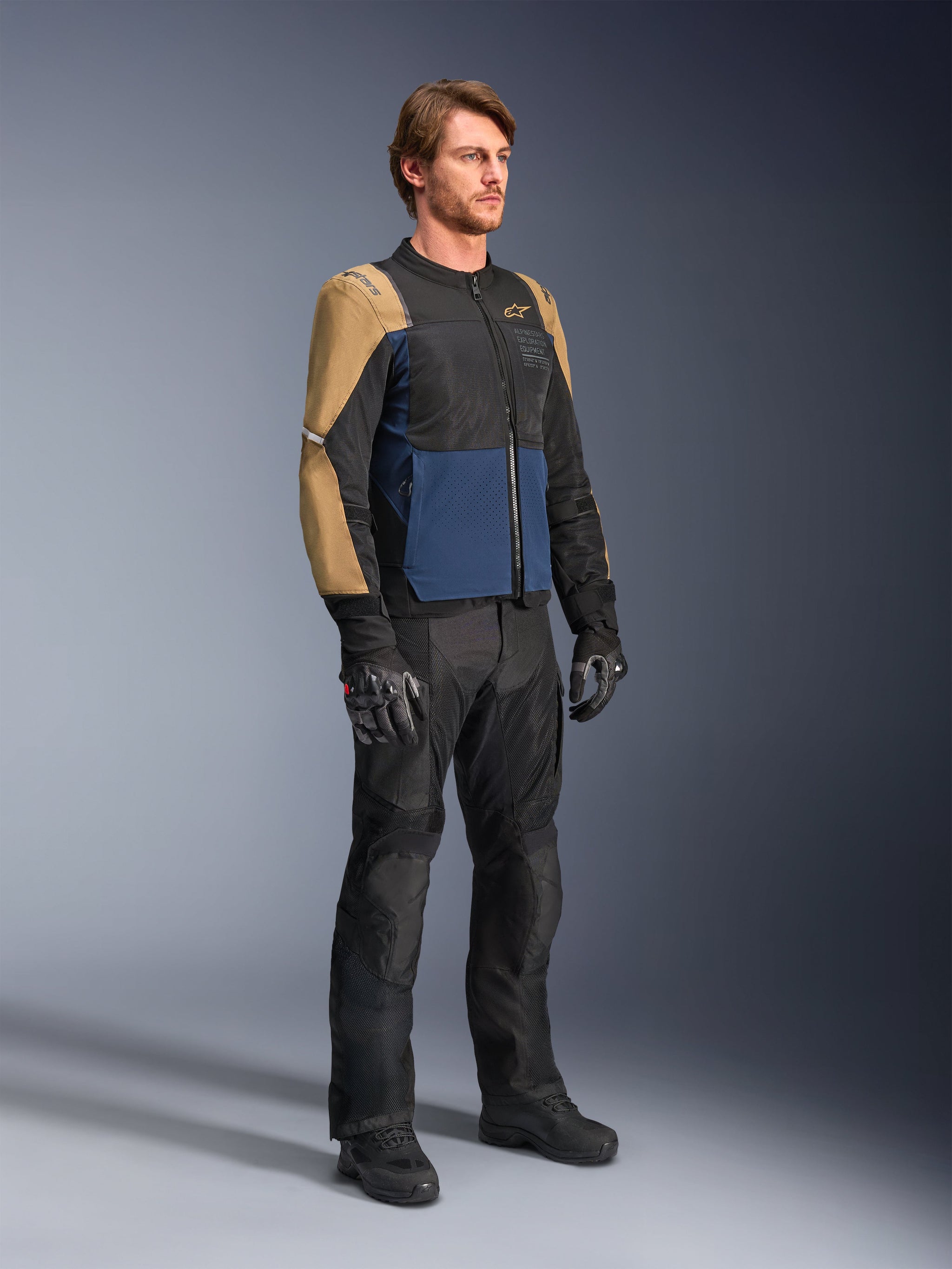 Male rider wearing the Alpinestars ST-2 Air Jacket in Deep Blue, Dark Khaki, and Black, featuring large mesh panels and laser perforations, paired with black riding pants, gloves, and boots for a complete summer touring look.