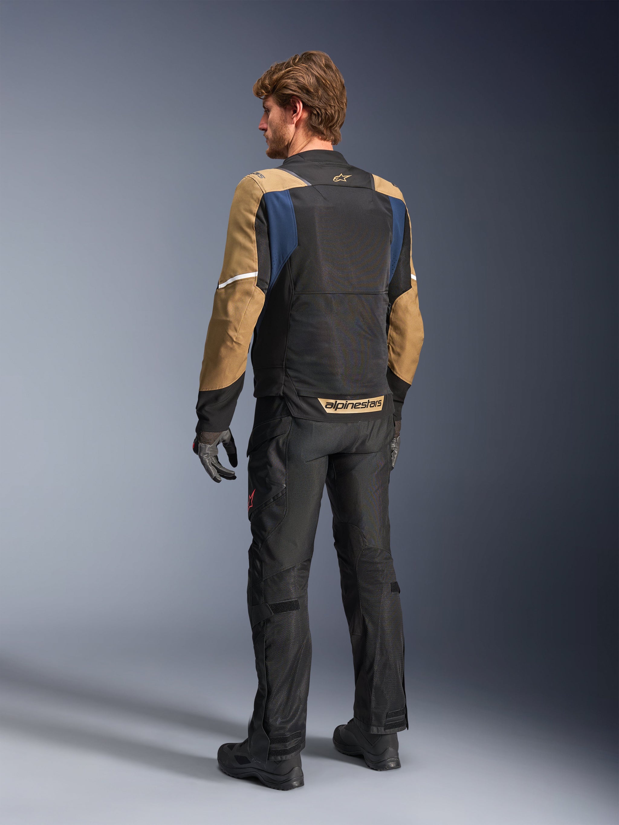 Alpinestars ST-2 Air Jacket, summer touring motorcycle jacket, Deep Blue, Dark Khaki, and Black, back view on model showing mesh panels, khaki sleeves, and blue accents, featuring white reflective strips and bold branding on the lower back, paired with black riding pants