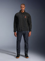 Alpinestars Revved WR Jacket in Black, worn by a model with dark blue jeans and black sneakers, front view, featuring snap button closure and a 3D embroidered logo on the chest, urban contemporary motorcycle gear.