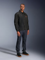 Alpinestars Revved WR Jacket in Black, urban coaches-style motorcycle jacket worn by a model with dark blue jeans and black sneakers, featuring a snap-button front and embroidered logo, minimalist and sporty design for road riding.