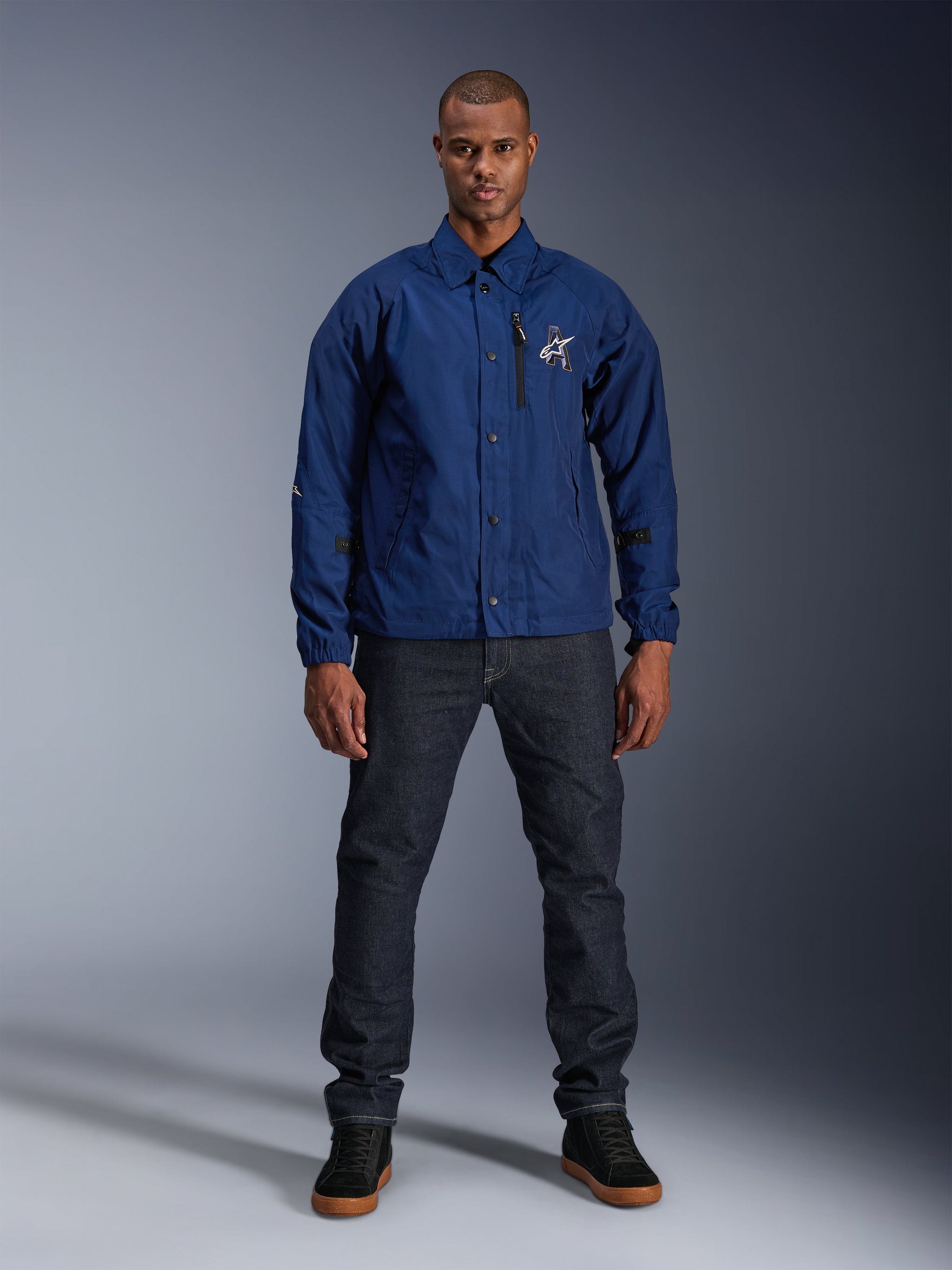 Alpinestars Revved WR Jacket, Navy Blue, coaches-style motorcycle jacket, worn by a man with dark denim jeans and black sneakers, featuring snap button closure and 3D Alpinestars logo, urban contemporary streetwear
