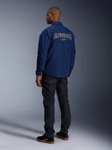 Model wearing the Alpinestars Revved WR Jacket in Navy Blue from behind, featuring large white outlined 'ALPINESTARS' embroidery across the back, paired with dark denim pants and black sneakers, urban motorcycle aesthetic.