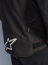 Alpinestars T-GP R V3 Drystar® Jacket, Black and White, close-up view of the lower back section featuring a large white Alpinestars star logo, a side zippered pocket with a red pull tab, and a velcro waist adjustment strap, durable textile material.