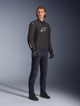 Male model wearing Alpinestars SMX Waterproof Jacket, Black with white and red logo accents, styled with dark blue denim pants and black riding gloves, sleek sport-fit textile motorcycle jacket.