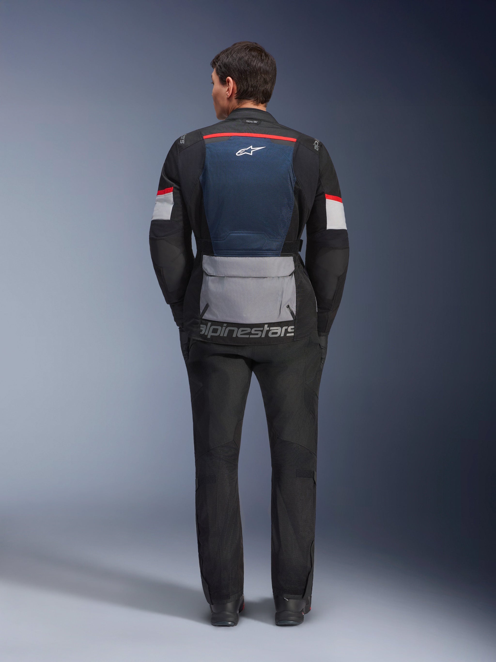 Alpinestars Andes Air Drystar Jacket, Deep Blue Black Ice Gray, rear view on model, featuring blue mesh back panel for ventilation, large gray lower pocket, red and white sleeve accents, 'alpinestars' wordmark, paired with black motorcycle pants for a complete touring outfit