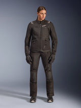 Female rider wearing Alpinestars Stella Andes V4 Drystar® Jacket in Black, paired with matching black adventure-touring pants and gloves, featuring technical textile construction with multiple utility pockets and white Alpinestars branding, complete all-weather motorcycle gear