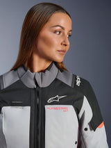 Close-up of a woman wearing the Alpinestars Stella Andes V4 Drystar® Jacket in Dark Gray, Ice Gray, and Coral Fluo, featuring the Astar logo and branding, hydration loop detail, and technical textile construction for adventure riding.