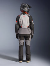 Woman wearing Alpinestars Stella Andes V4 Drystar® Jacket from the back, Dark Gray, Ice Gray, Black, and Coral Fluo accents, matching adventure pants and black helmet, multi-paneled textile design for touring and all-weather performance