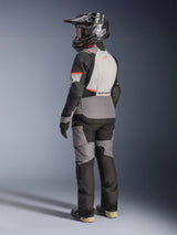 Alpinestars Stella Andes V4 Drystar® Jacket, Women's Motorcycle Jacket, Dark Gray/Ice Gray/Black/Coral Fluo, three-quarter rear view of a rider in full gear, featuring Alpinestars branding on the back, elongated hem, and durable textile construction, coordinated with matching pants and off-road boots for adventure riding