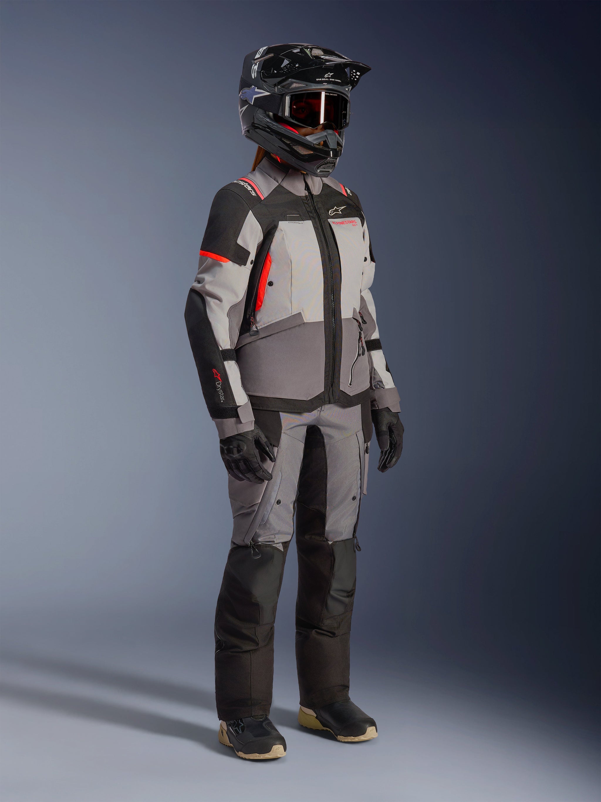 Alpinestars Stella Andes V4 Drystar® Jacket, Women's Adventure Motorcycle Jacket, Dark Gray Ice Gray and Black with Coral Fluo accents, worn by a rider in a full gear set with matching gray pants, black adventure helmet with goggles, and black gloves.