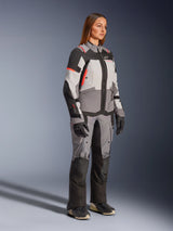 Female model wearing the Alpinestars Stella Andes V4 Drystar® Jacket in Dark Gray, Ice Gray, and Black with Coral Fluo accents, paired with matching adventure riding pants and black gloves, professional waterproof motorcycle gear for women.