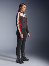 Female model standing in a side profile wearing the Alpinestars Stella T-Dyno WR Jacket in Black, Ecru, and Bright Red, featuring racing stripes on the sleeves and star logos, paired with black pants and lace-up boots for an urban motorcycle style.