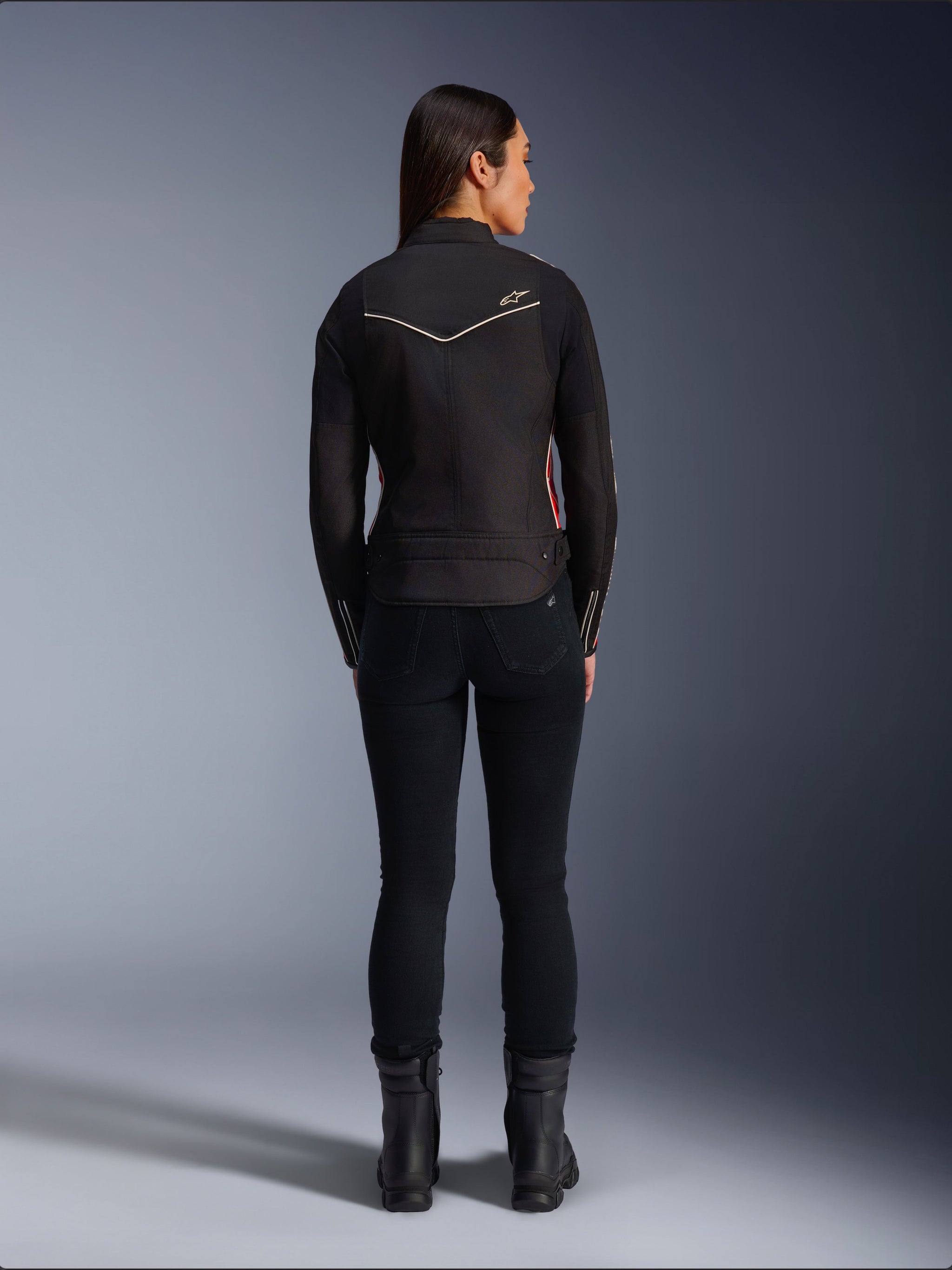 Female model from behind wearing Alpinestars Stella T-Dyno WR Jacket in Black Bright Red Fuchsia, textile motorcycle jacket with a shorter biker fit, rear view showing white star logo, styled with black pants and black boots