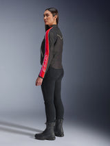 Female model wearing the Alpinestars Stella T-Dyno WR Jacket in Black Bright Red Fuchsia, featuring bold red and pink stripes with Alpinestars branding on the sleeve, paired with black riding pants and black motorcycle boots in a studio setting.