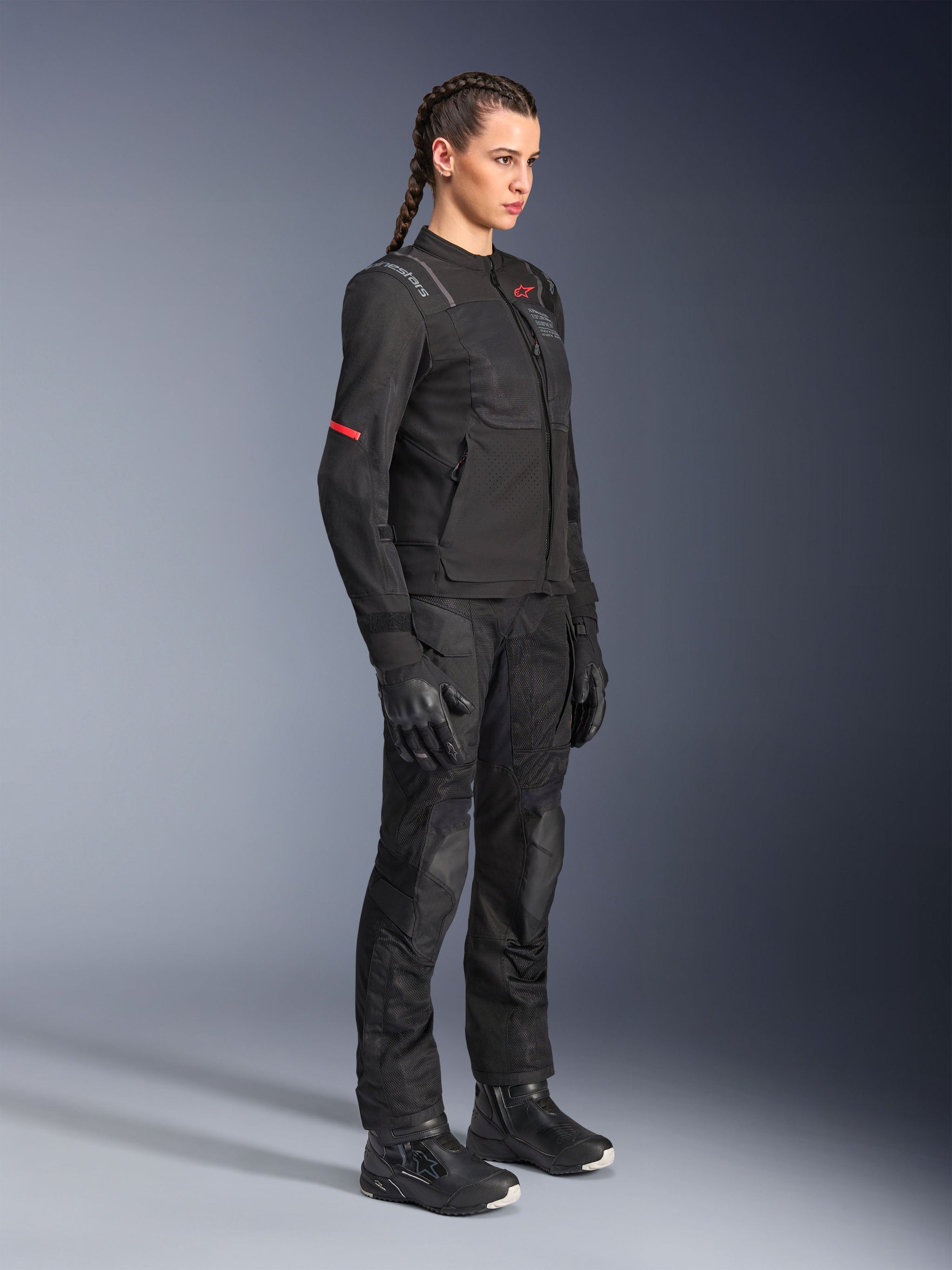Female model wearing the Alpinestars Stella ST-2 Air Jacket in Black, paired with matching black motorcycle pants, gloves, and boots, featuring mesh ventilation panels and subtle red details, sleek modern touring outfit