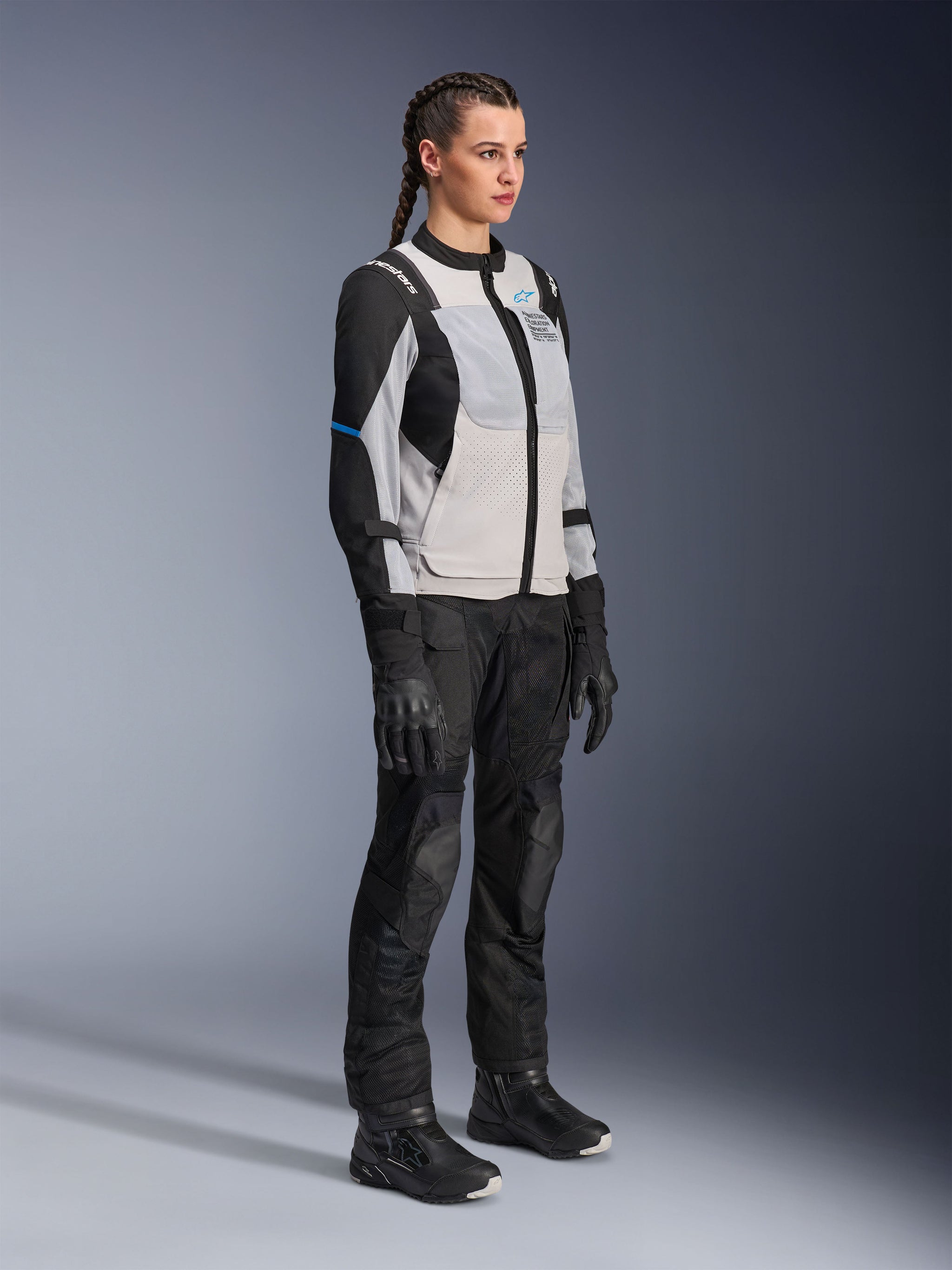 Model wearing the Alpinestars Stella ST-2 Air Jacket in Ice Gray and Black, women's technical motorcycle jacket with mesh panels and softshell construction, paired with black adventure touring pants and boots, featuring blue accents and a modern riding design