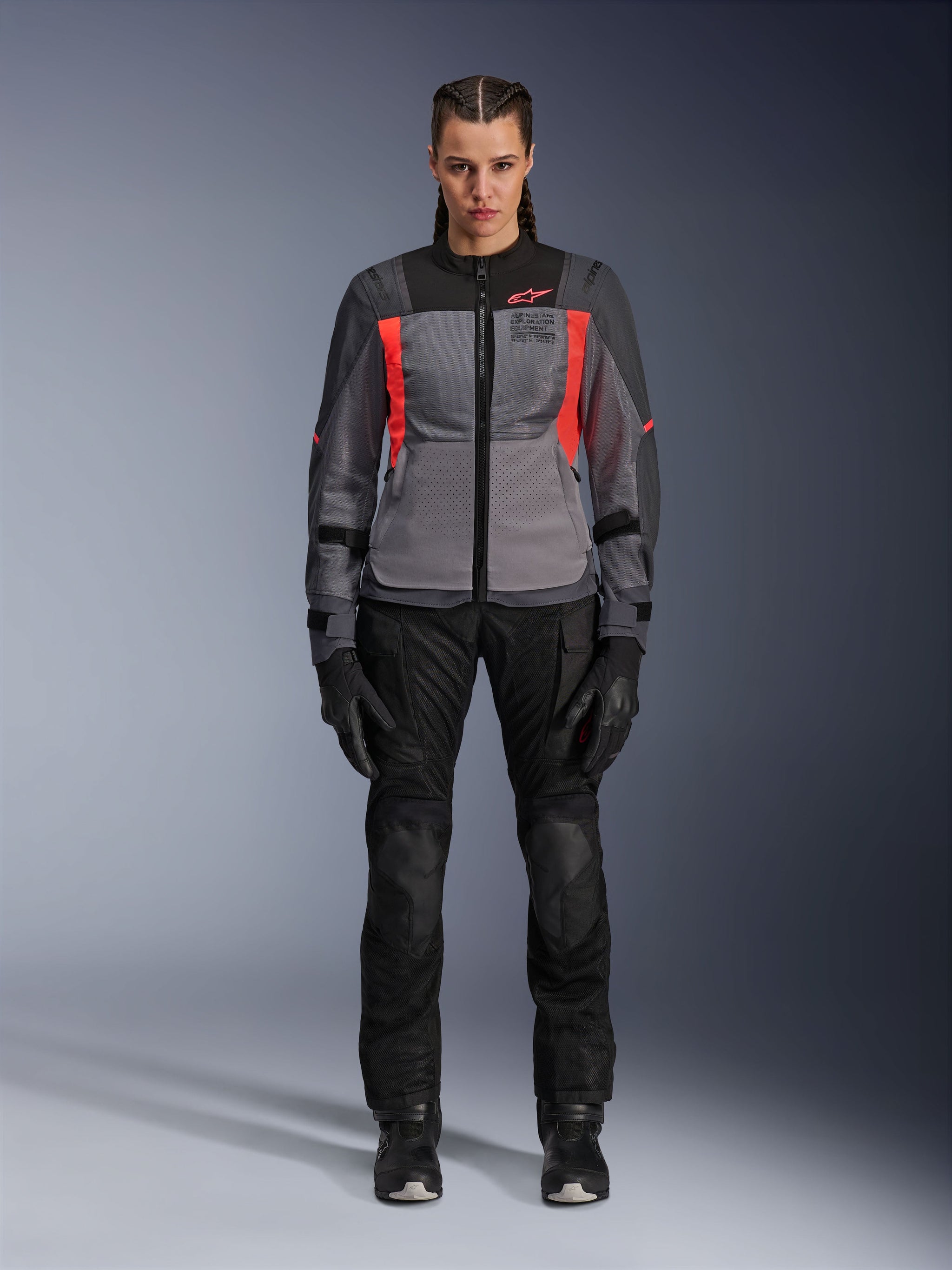 Woman wearing Alpinestars Stella ST-2 Air Jacket in Deep Gray, Dark Gray, and Fluo Coral, paired with black motorcycle pants and gloves, front view, modern mesh adventure touring gear for women