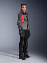 Woman rider wearing the Alpinestars Stella ST-2 Air Jacket in Deep Gray, Dark Gray, and Fluo Coral, paired with black motorcycle pants, gloves, and boots, featuring a modern touring design with mesh panels and reflective details.