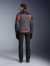 Rear view of a model wearing the Alpinestars Woman Stella St-2 Air Jacket in Deep Gray and Dark Gray with Fluo Coral accents, featuring large mesh ventilation panels on the back and reflective logo details, paired with black motorcycle pants and gloves.