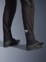 Alpinestars Aeroshell Pants, Black softshell motorcycle pants, close-up of lower leg and elasticated hem, white Alpinestars logo on calf, styled with black riding shoes, modern crossover sport design