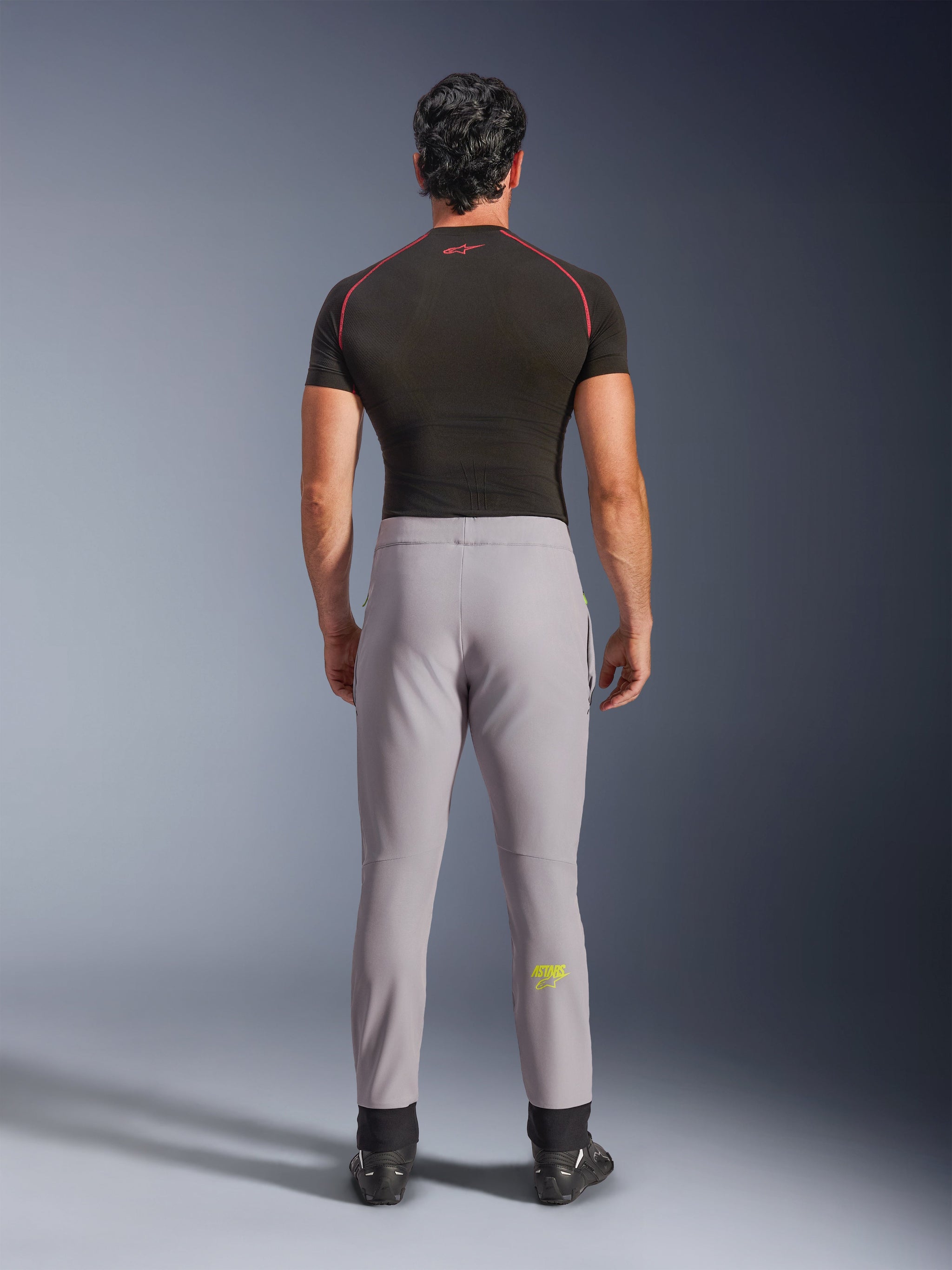 Alpinestars Aeroshell Pants, Mid Gray with Yellow Fluo logo, rear view of crossover sports softshell motorcycle pants, worn with a black compression shirt and riding shoes, featuring an elastic waist and tapered silhouette.