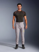 Male model wearing Alpinestars Aeroshell Pants in Mid Gray and Yellow Fluo, crossover sports softshell pants with elastic drawstring waist and zippered pockets, paired with a black short-sleeved performance shirt, modern athletic design for road and casual riding