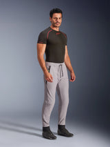 Alpinestars Aeroshell Pants, Mid Gray with Yellow Fluo accents, crossover softshell pants worn by a model with a black base layer and black shoes, featuring a modern tapered fit, elastic waistband with black drawcord, and zipped pockets.