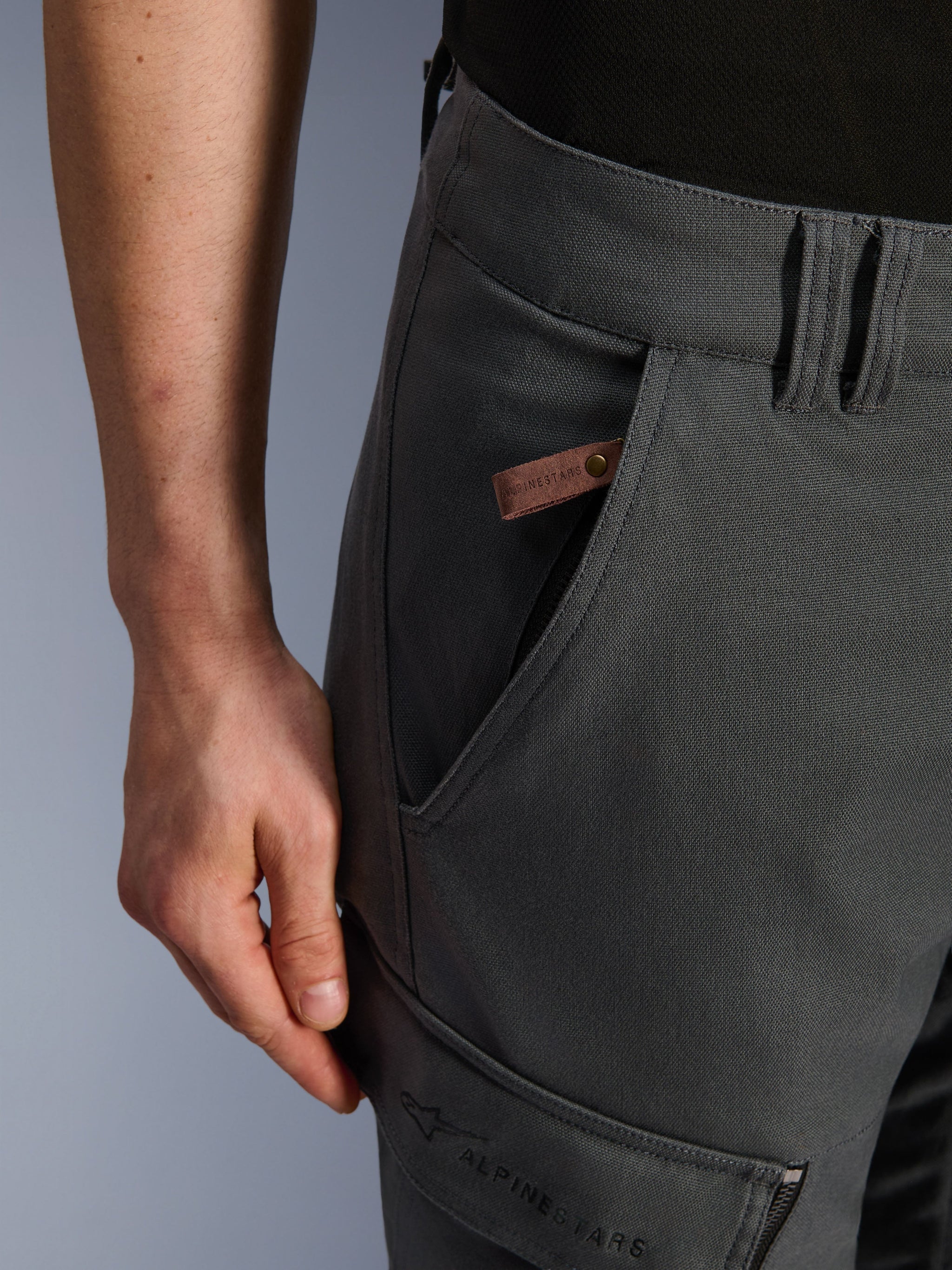 Alpinestars Borrego Drystar® Pants, Adventure Motorcycle Pants, Anthracite Gray, close-up detail of the pocket and hip, waxed-canvas texture with a brown leather logo tag and embroidered Alpinestars branding on the thigh cargo pocket.