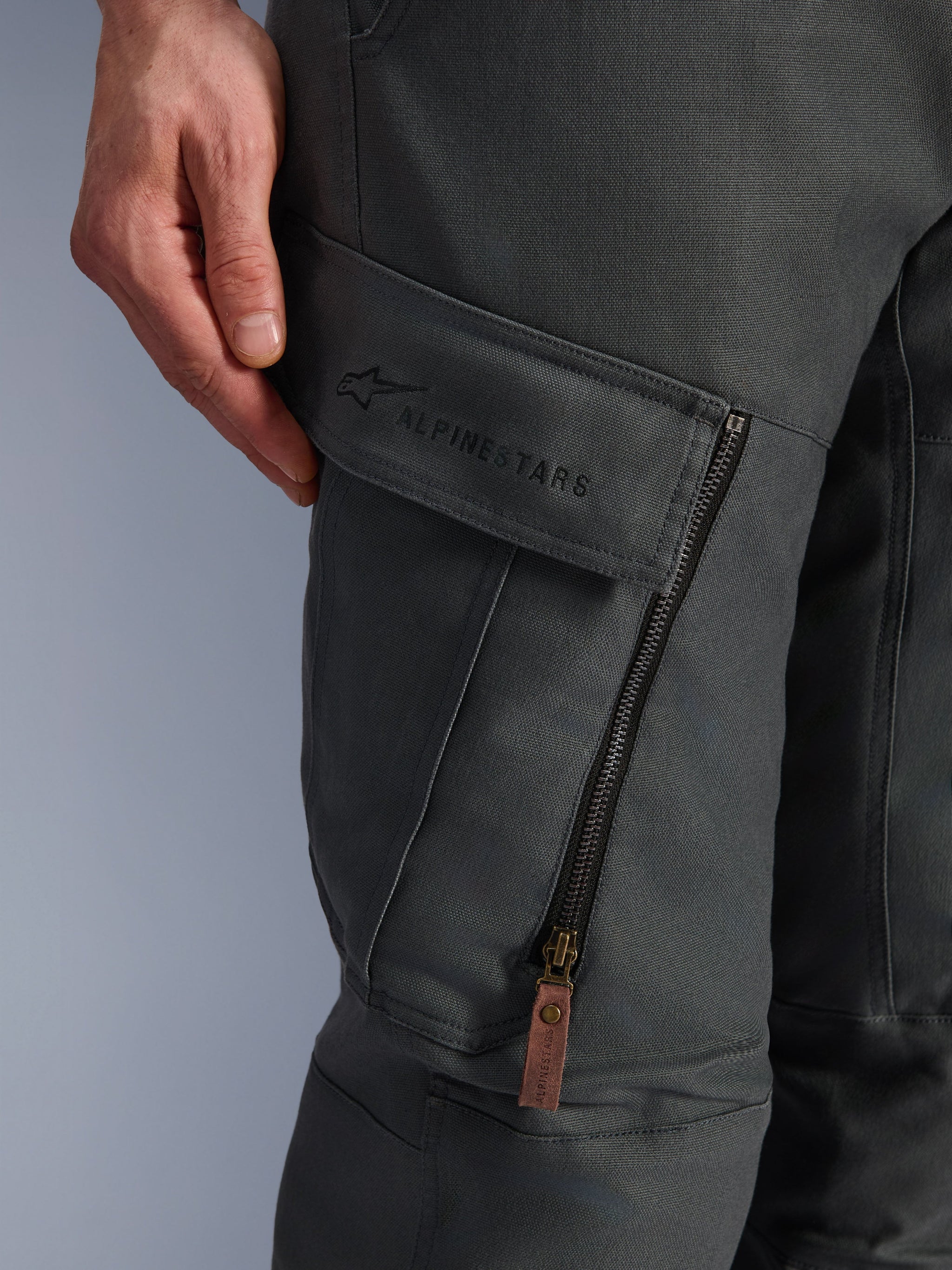 Alpinestars Borrego Drystar® Pants, Anthracite Gray, close-up of thigh cargo pocket with embroidered branding, textured waxed-canvas material, vertical ventilation zipper with a brown leather pull tab