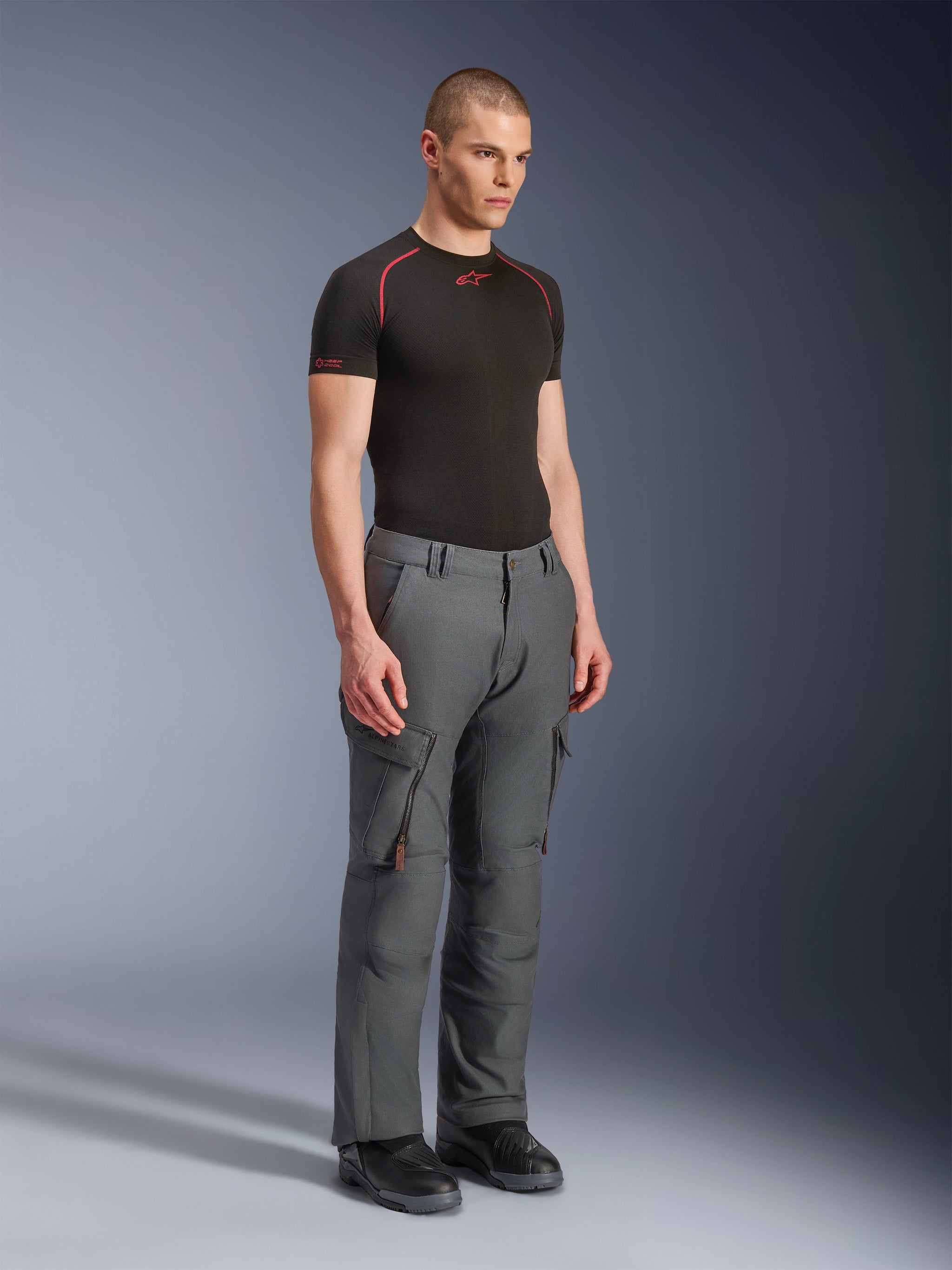 Male model wearing Alpinestars Borrego Drystar® Pants, Gray Anthracite adventure motorcycle pants, workwear-inspired design with cargo pockets and zippered vents, styled with a black short-sleeve base layer and black boots