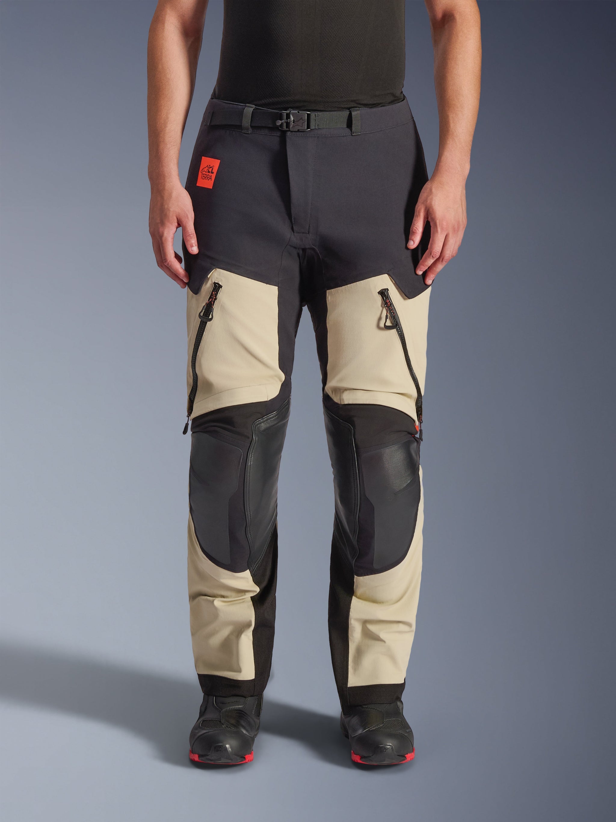 Alpinestars Halo Pro Drystar® XF Laminated Pants, Adventure Motorcycle Pants, Mastic Black, front view worn by a rider, featuring large zippered thigh vents, reinforced black knee panels, and tan textile construction, paired with black and red riding boots